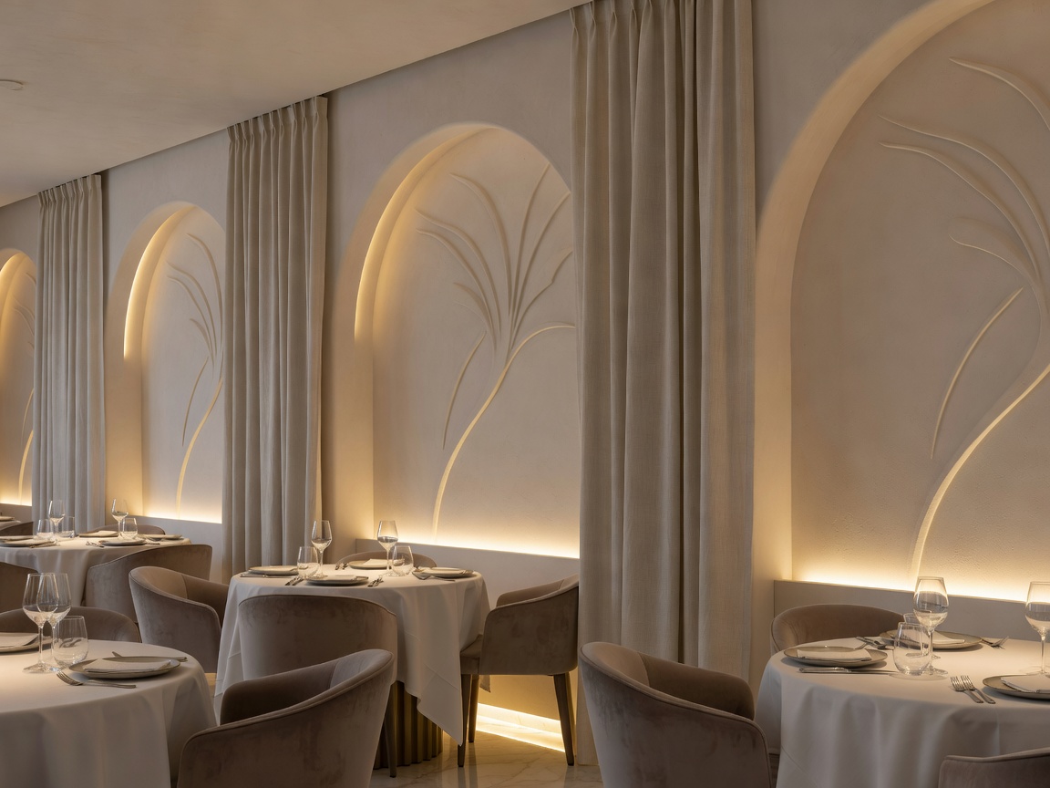 Refined restaurant interior with sculpted plaster alcoves, linen drapes, and warm low-level architectural illumination